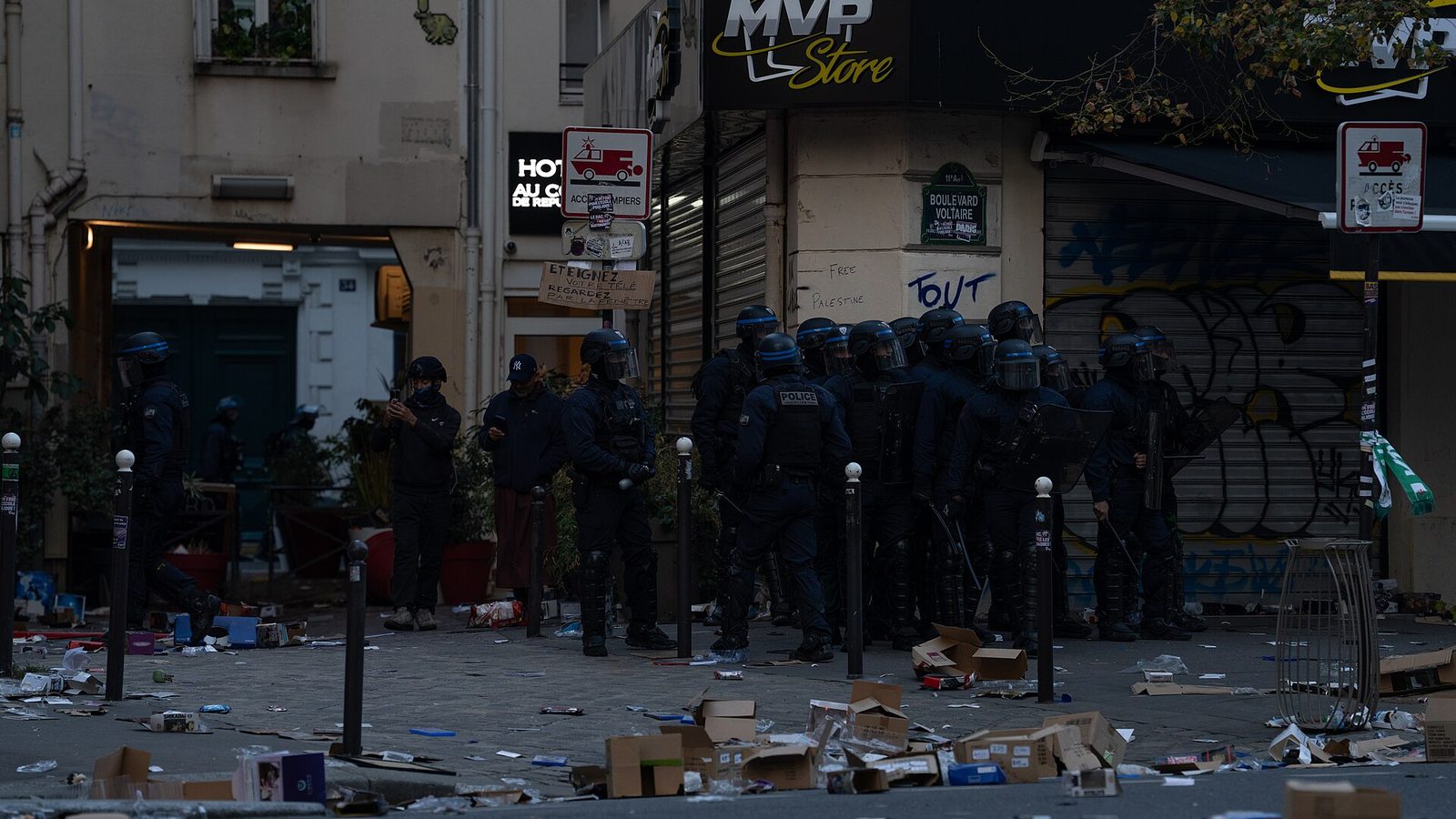 Policiers casqués devant une boutique pillée, boulevard Voltaire à Paris, cartons et débris éparpillés sur la chaussée