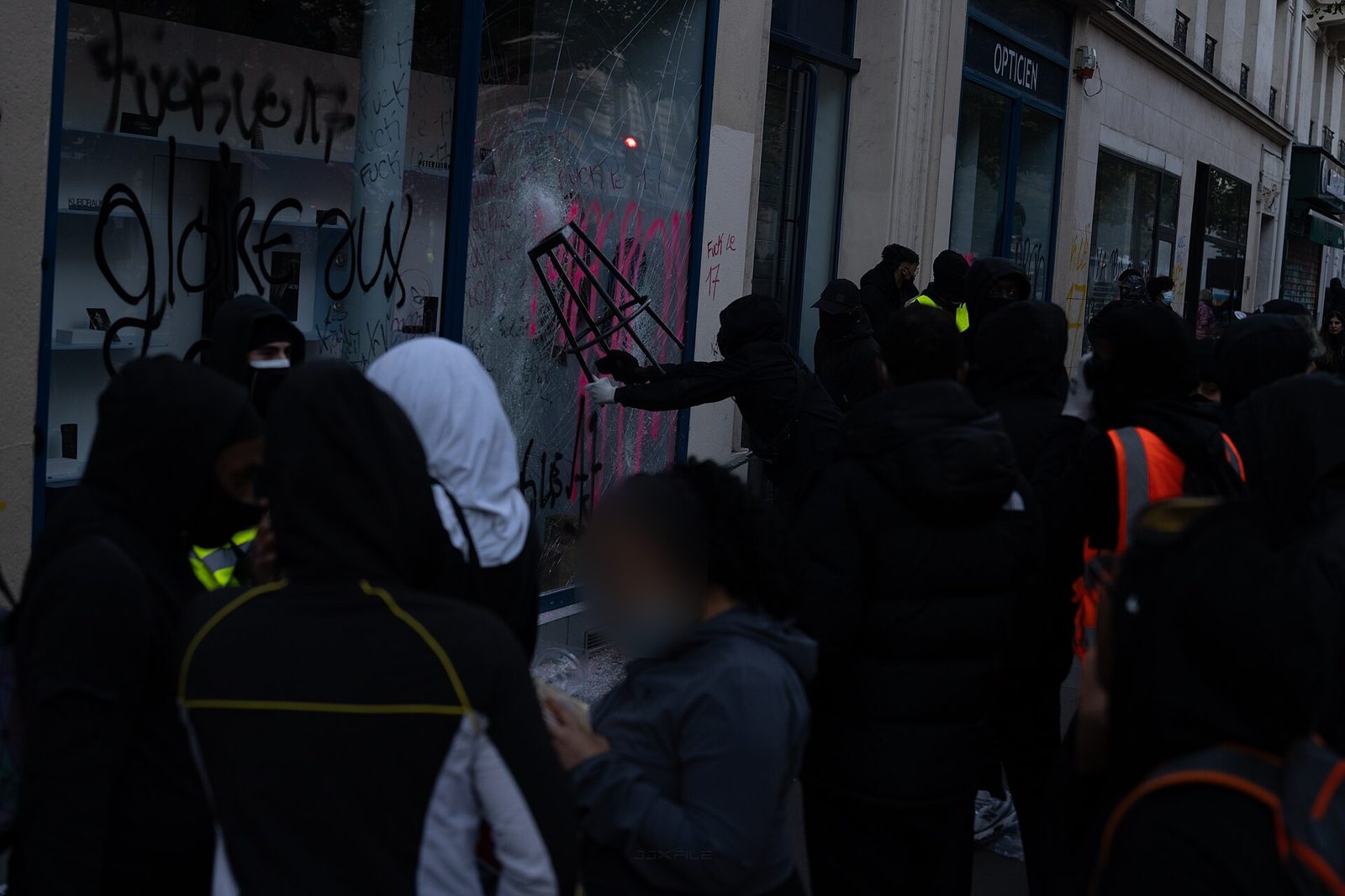 Un individu masqué frappe une vitrine taguée avec une chaise de terrasse, au milieu d'un groupe, à Paris le 17 octobre 2026